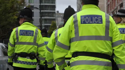 Police officers wearing hi-vis jackets. Photo is taken from behind. 