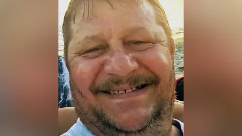 A man with brown hair and long brown facial hair smiles at the camera.