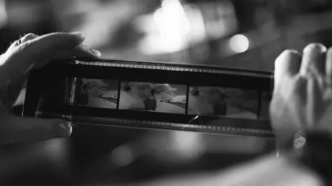 Katie Simmons A black and white photo of someone handling a reel of film used in the cinema