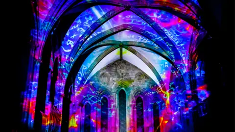 A cathedral ceiling lit up in blue, pink, purple and green lights