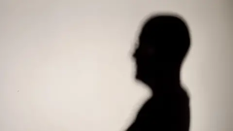 A black shadow outline of a person against a white wall. 