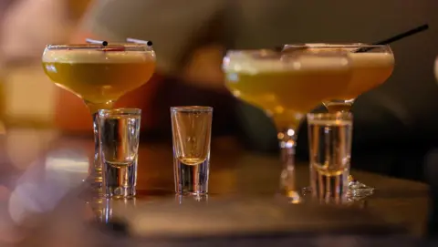 PA Media Three cocktail drinks alongside three shot glasses. The cocktail glasses have straws on them or in them.