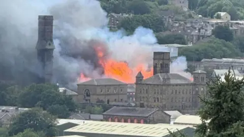 Robbie Moore A large blaze engulfs a Victorian mill building. The view is from a distance