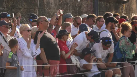 Royal Navy Crowds of people, some with phones out, in the evening sun