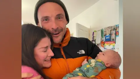 A mum and dad holding a baby.