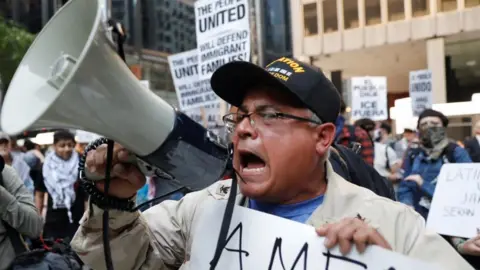 A man screams into a bullhorn wearing a US Navy hat in Chicago.