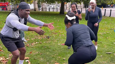 Danai Nesta Kupemba / BBC A man and a woman wearing running gear dance in Hyde Park