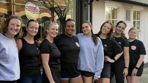Pia Carson-Moore Pia Carson-Moore stands in the middle of a group of women who are all smiling at the camera. They are all wearing active/running clothing. Some of them wear jumpers and shorts.