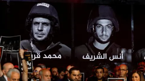 Black and white photographs of Al Jazeera journalists Mohammed Qreiqeh and Anas al-Sharif on a wall behind a group of Al Jazeera staff members who gathered to remember their colleagues at the network's studio.