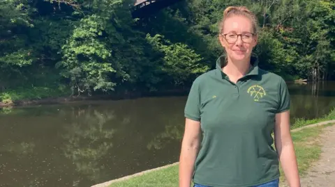 A woman in a green t-shirt and jeans standing by the River Severn
