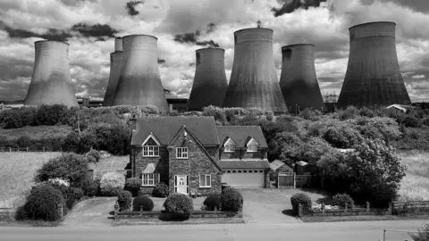 A house in front of Ratcliffe-on-Soar power station's cooling towers in black and white.