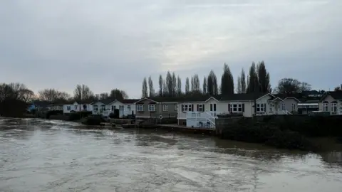 The River Stour at a very high level with a row of mobile homes at the far side of the river.