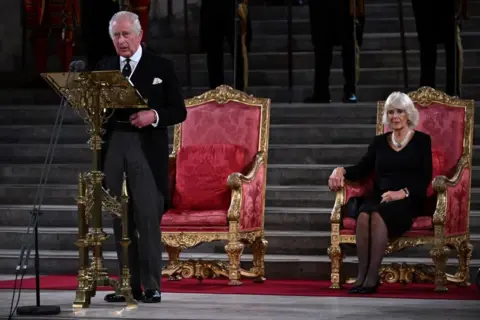 BEN STANSALL/AFP Britain's King Charles III, flanked by Britain's Camilla, Queen Consort, speaks during the presentation of Addresses