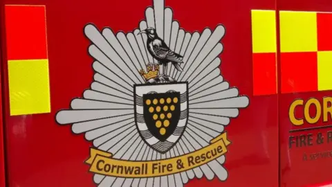 The Cornwall Fire and Rescue Service emblem on the side of a red fire engine.