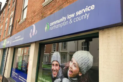 Laura Coffey/BBC The outside of a ground-floor commercial property. The blue and green branding, with white lettering, reads COMMUNITY LAW SERVICE NORTHAMPTON & COUNTY. Printed on the window are photos of a man and a woman smiling.