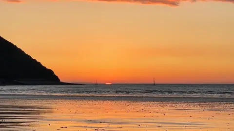 Weather Watchers/Sparky The sea can be seen from the beach. The sun is going down and only a sliver of orange remains on the horizon.