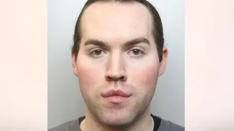 Cheshire Police A police mugshot of Jack Watkin. He has long brown hair which is tied back and is wearing a grey top with a dark coloured top underneath.