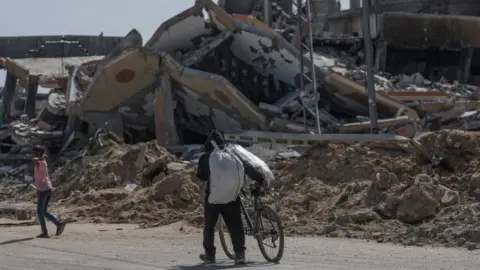 EPA A displaced Palestinian man pushes a bike along Salah al-Din road in southern Gaza after fleeing Rafah (9 May 2024)