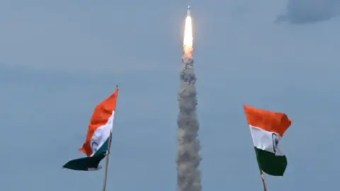 Getty Images People wave Indian flags as an Indian Space Research Organisation (ISRO) rocket carrying the Chandrayaan-3 spacecraft lifts off from the Satish Dhawan Space Centre in Sriharikota, an island off the coast of southern Andhra Pradesh state on July 14, 2023. India launched a rocket on July 14 carrying an unmanned spacecraft to land on the Moon, its second attempt to do so as its cut-price space programme seeks to reach new heights. (Photo by R.Satish BABU / AFP) (Photo by R.SATISH BABU/AFP via Getty Images)