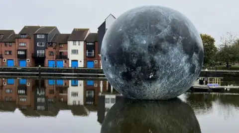 The Fallen Moon exhibit, which is a large moon according to NASA data, floating in the water at Bridgwater docks.