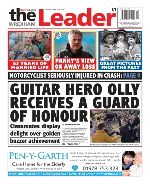 The Wrexham Leader The Wrexham Leader with a main headline reading: "Guitar hero Olly receives a guard of honour". A young boy gives a high five to another pupil as others stand in a row waiting to congratulate him. Above that are three smaller headlines: 65 years of married life with a picture of an elderly couple, Parky's view on away loss, and a picture of three girls in traditional Welsh costumes with the headline 'great pictures from the past'