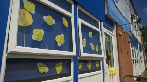 BBC Cardboard cut outs of yellow bees are displayed windows with white window frames and blue blinds behind.