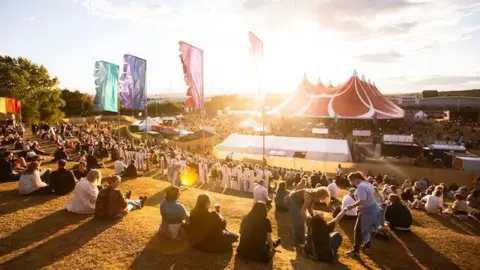 Rock N Roll Circus Crowds looking down a hill at a big tent at a festival.