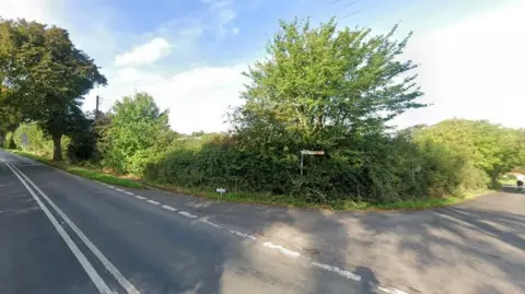 A junction on a country road with green trees and bushes.