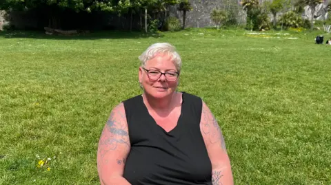 Lindsay Soper sat on a grass area. She is wearing a black top and is smiling at the camera.