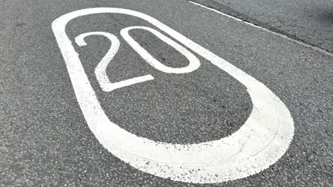 Generic 20 mile per hour white sign on the grey tarmac road