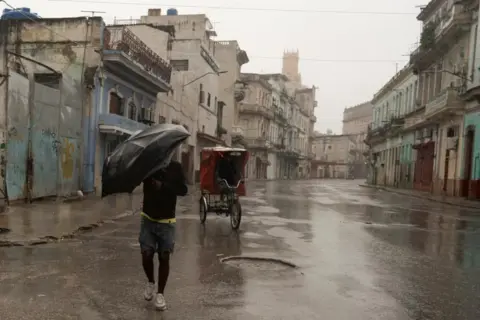 Reuters A man seen walking under an umbrella during heavy rains in Havana.