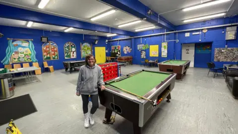 A woman wearing a hoodie standing next to a pool table