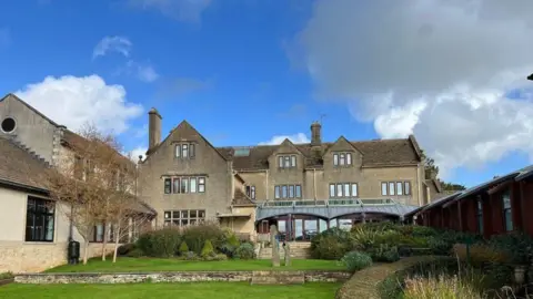 Dorothy House's base in Winsley, as seen from the back showing the garden. It is a large three-storey house with extensions and a glass conservatory.