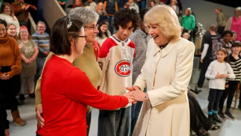 PA Media The Queen holds an actors hand in hers and is smiling. People are standing around them.