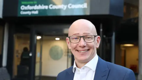 Oxfordshire County Council Dr Martin Reeves smiling for a picture in front of Oxfordshire County Council headquarters.