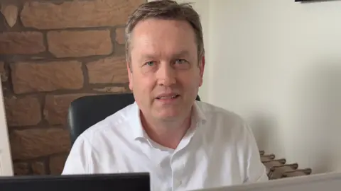 Graham Poles A man in a white shirt looking over his computer screen