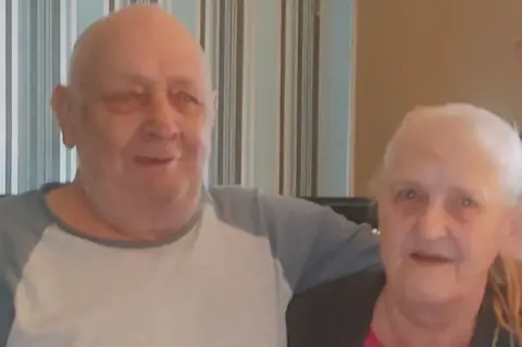 Stewart Bell An elderly couple, John and Susan Bell, standing with arms around each other