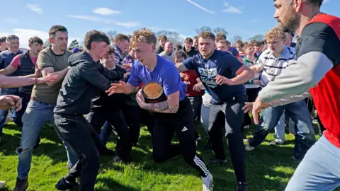 PA Media A man running in front of a crowd of people whilst playing bottle kicking in Leicestershire