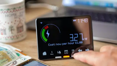 Getty Images A smart meter display on a table with a mug, £5 notes and a smartphone alongside it.
