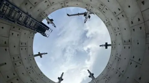 View from inside a large sewer pipe, looking up to the sky.