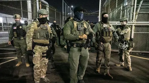 U.S. Immigration and Customs Enforcement (ICE) agents stand in front of chain link fence