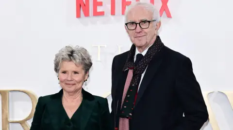 Getty Images A woman and a man stood next to each other at a film premier. They both have short grey hair and are wearing dark suits.