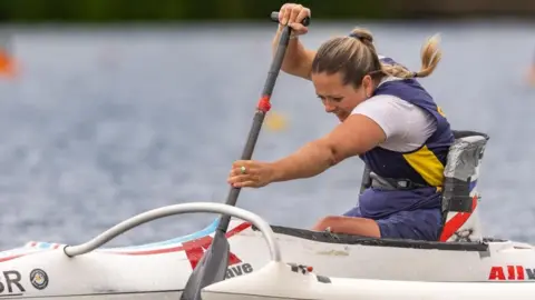 A woman with long blonde hair tied back in a plait paddles in an adapted canoe.