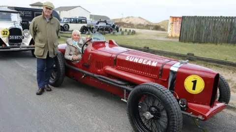 Michael Ashcroft Lieutenant Colonel Stephen Segrave, great nephew of Sir Henry Segrave and Gina Campbell, daughter of Donald Campbell and granddaughter of Major Sir Malcolm Campbell, pictured at Ainsdale in 2016, with the Sunbeam Tiger. It is bright red in colour and a single-seater.