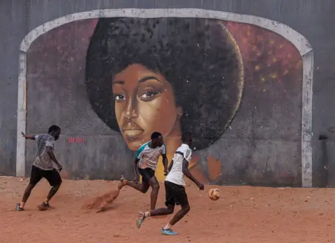 ZOHRA BENSEMRA / REUTERS Men play soccer near a graffiti mural showing a woman with a perfectly round Afro, in Yoff, a neighbourhood of Dakar.