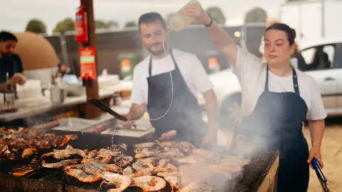 @Maddiemonet Two people grilling lobster on an large outdoor grill.