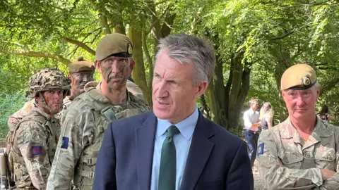 A man in a suit stood in front of people in camouflage soldier outfits.