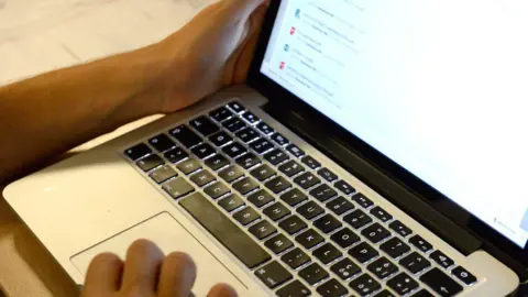 Dino Panato/Getty Images A laptop which is open. The screen is on, and there are two hands visible - one is touching the trackpad, the other the screen.