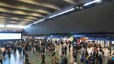 PA Media A view of the large advertising board at Euston train station in north London, which has been switched off by Network Rail with passengers viewed in the main hall