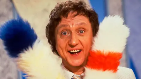 Getty Images Ken Dodd's face between two colourful tickling sticks in 1986